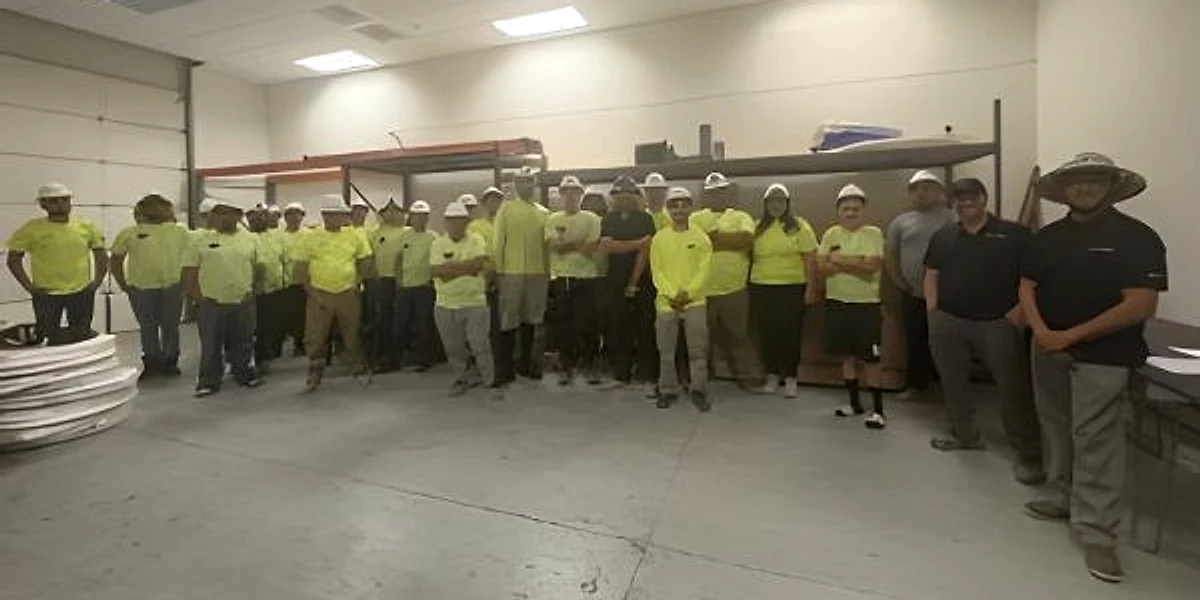 The full Ancla Plumbing crew lined up in the warehouse in safety-yellow shirts and hard hats