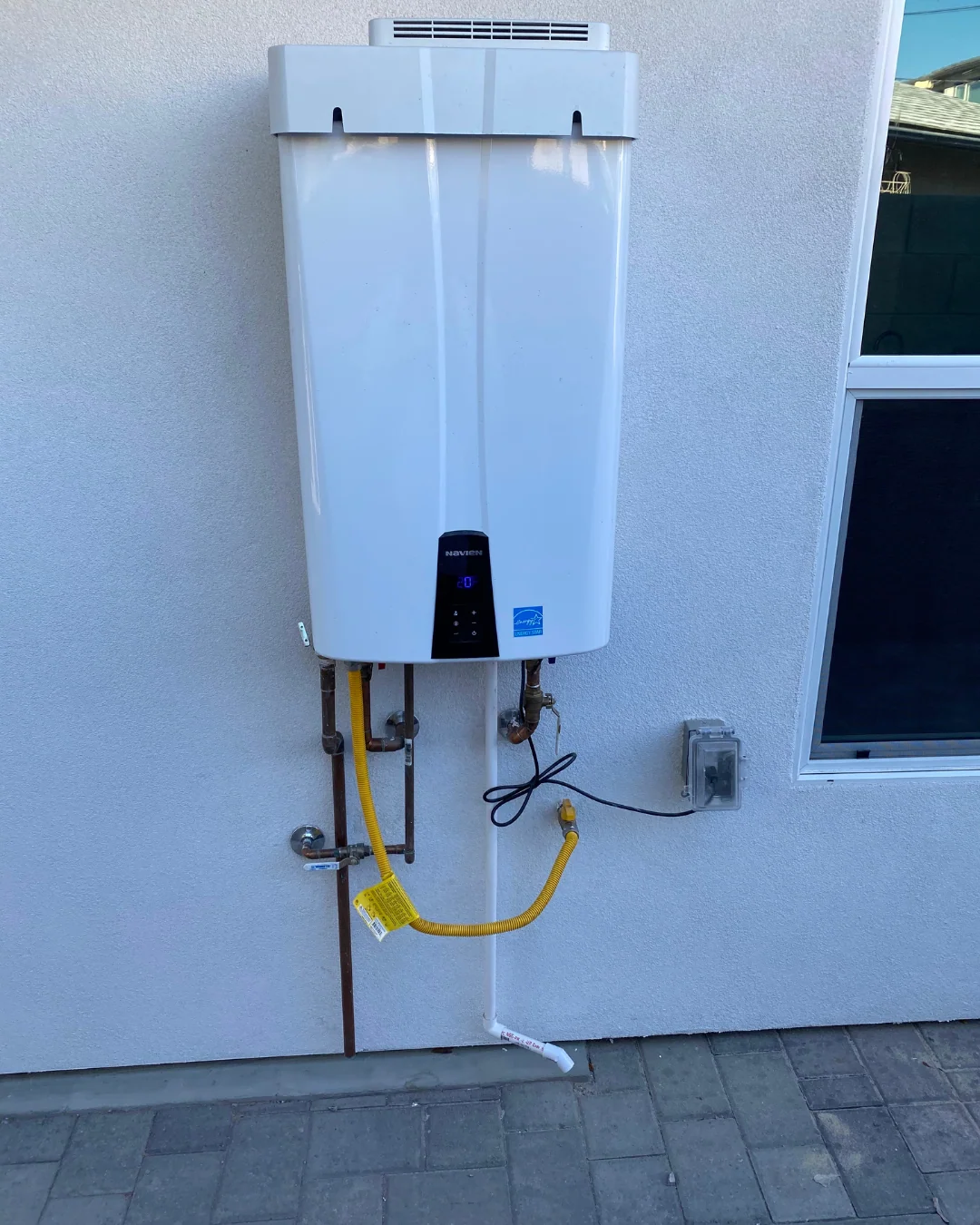 Navien tankless water heater installed on an exterior stucco wall with gas and water lines neatly run