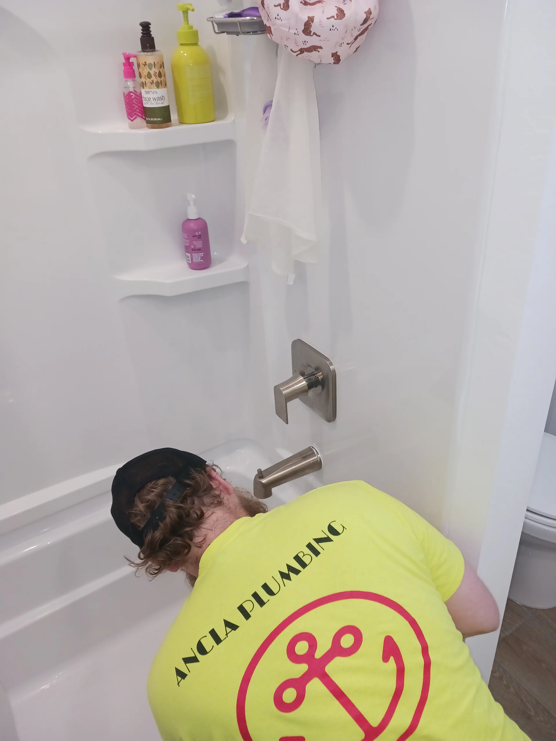 Ancla plumber in a yellow Ancla Plumbing tee setting fixtures inside an alcove tub-shower