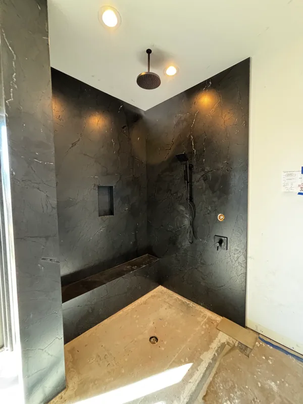 Walk-in shower with black veined marble walls and bench, matte-black handheld and rain showerheads, and recessed ceiling lights overhead