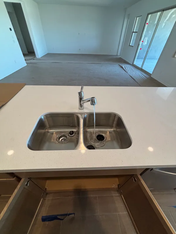 Stainless double-bowl undermount kitchen sink in a white quartz counter with a chrome pull-down faucet running water during commissioning
