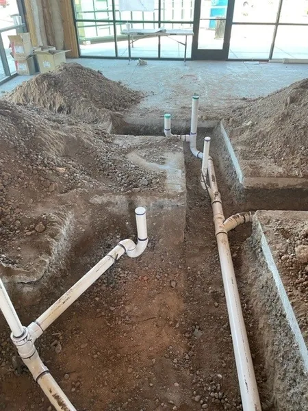 Multiple PVC drain stub-outs set in a sand trench at a glass-walled commercial new-construction site
