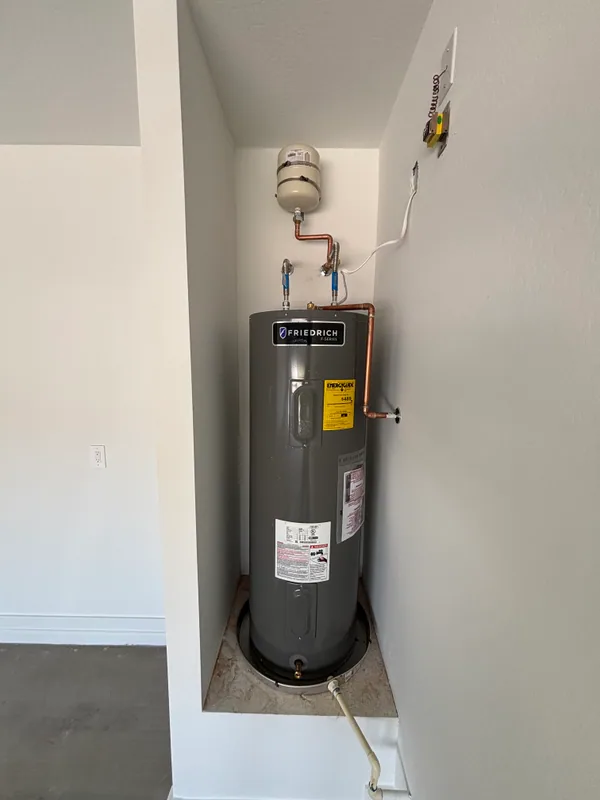 Friedrich gas-fired tank water heater installed in a closet with copper supply lines, expansion tank, and PVC vent to the ceiling