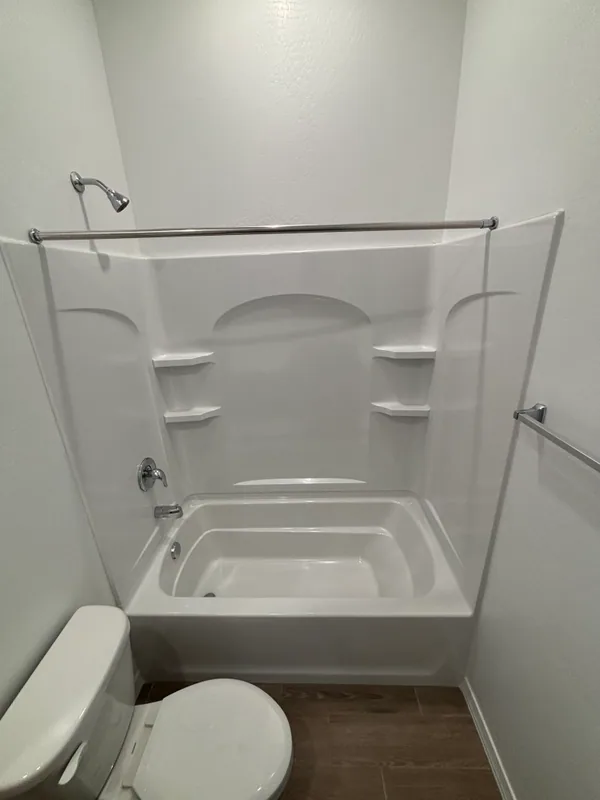 White acrylic garden tub-and-shower combo with chrome curtain rod, handheld sprayer, and tub filler, set against a wood-look tile wall