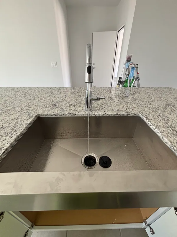 Stainless undermount kitchen sink in a speckled granite island with a chrome pull-down faucet running water over the disposal flange
