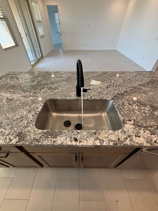 Stainless undermount kitchen sink in a dark speckled granite island with a matte-black single-handle pull-down faucet and subway-tile wall behind