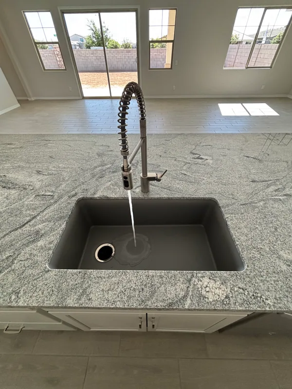 Black pro-style spring kitchen faucet over a deep gray composite sink set in a veined granite counter, with tall arched windows behind