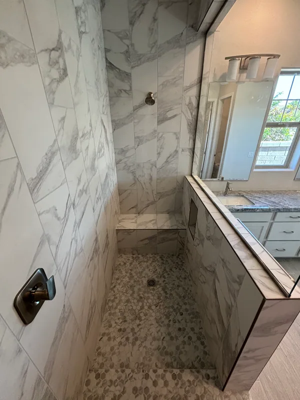 Marble-tiled bathroom showing a tub deck with bronze tub spout, hexagon mosaic accent on the back wall, and matching marble floor tile
