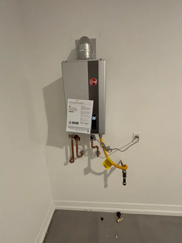 Rheem tankless water heater mounted on an interior wall with PVC venting, copper supply lines, and a yellow flex gas connector