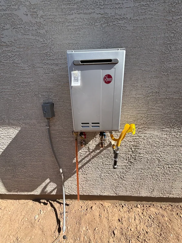 Rinnai tankless water heater mounted on a tan stucco exterior wall with copper supply lines, gas shutoff, and a sediment trap