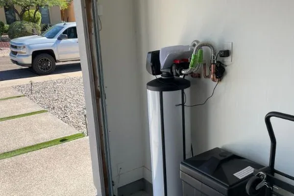 Water softener installed near an open garage door with copper supply lines and a service truck in the driveway