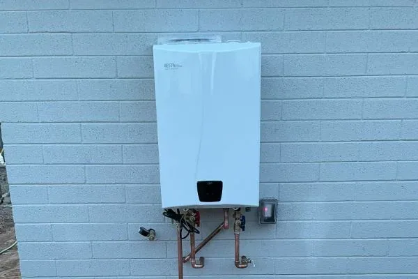 Tankless water heater mounted on a cinder-block exterior wall with copper supply lines