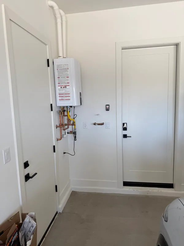 White tankless water heater on a garage wall with twin vent flues and copper gas-and-water service lines