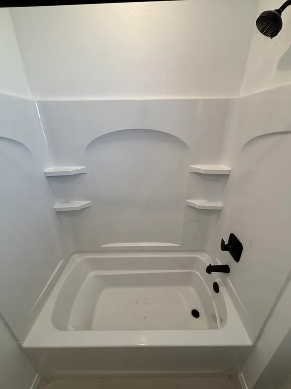 White acrylic alcove tub-and-shower surround with matte-black showerhead, valve trim, and tub spout, fresh from install