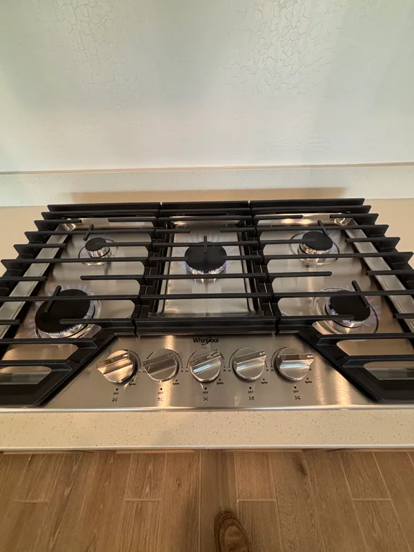 Stainless Whirlpool five-burner gas cooktop set into a quartz counter with cast-iron grates and chrome control knobs